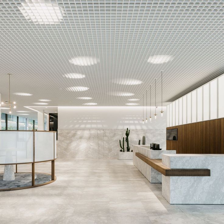 an empty lobby with white walls and wooden benches in the center, along with potted cacti