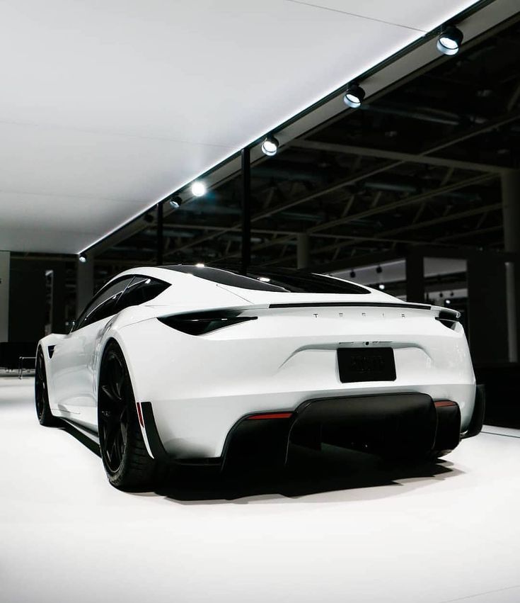 a white sports car parked in a showroom with lights on the ceiling and floor