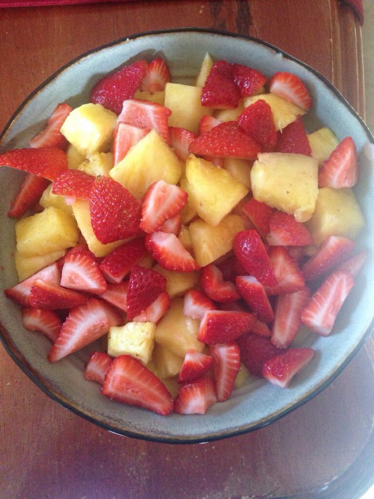 a bowl filled with sliced up strawberries and pineapples on top of a wooden table