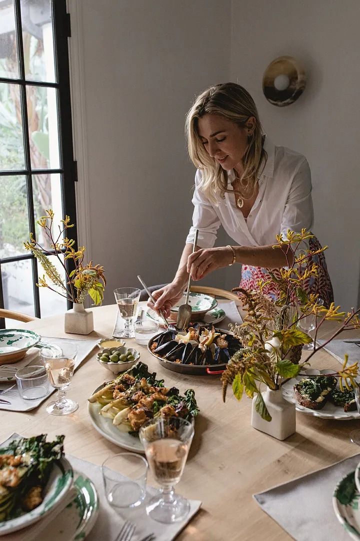 a woman sitting at a table in front of plates of food and flowers on the table