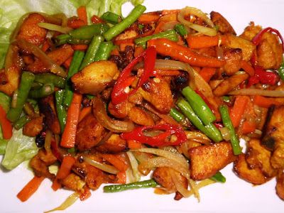 a white plate topped with chicken and veggies next to lettuce covered in sauce