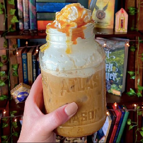 a hand holding a mason jar filled with liquid and topped with whipped cream, caramel and orange peels