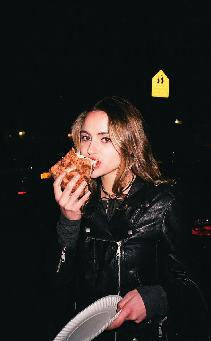 a woman eating a slice of pizza at night