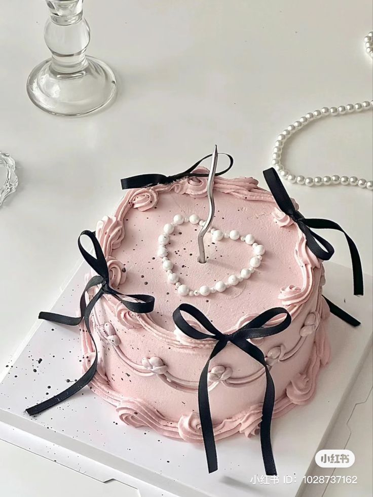 a pink cake decorated with pearls and a heart shaped candle sits on a white table