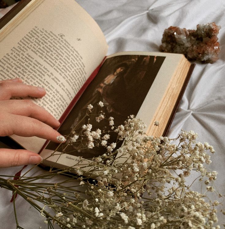 a person is holding an open book with flowers in front of them on a bed