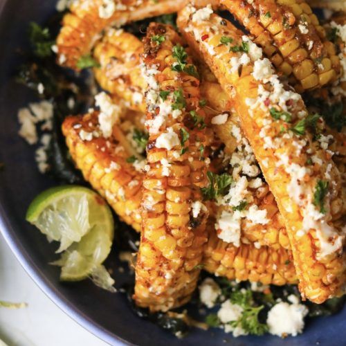 a blue plate topped with grilled corn and vegetables