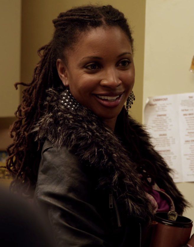 a woman with dreadlocks holding a coffee cup in her hand and smiling at the camera