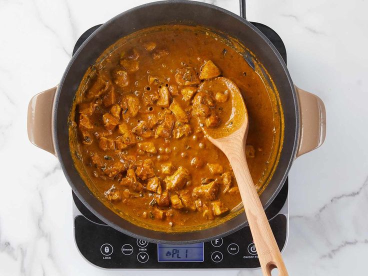 a wooden spoon in a pot filled with stew on top of an electric stovetop