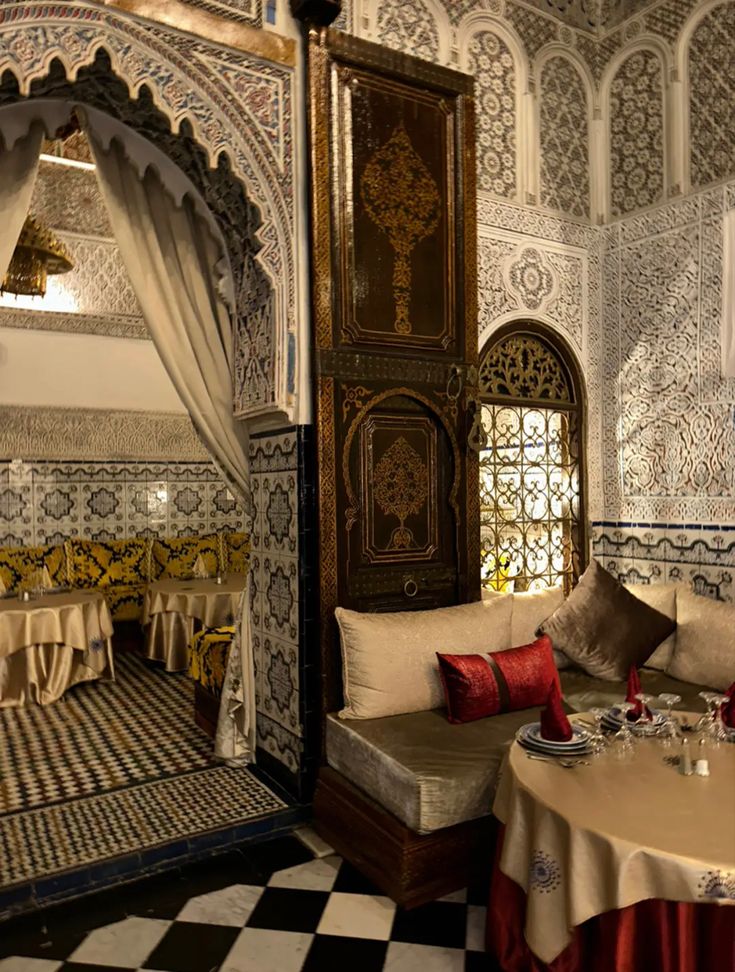 the interior of an ornately decorated restaurant with white and gold walls, black and white checkered flooring, and red pillows