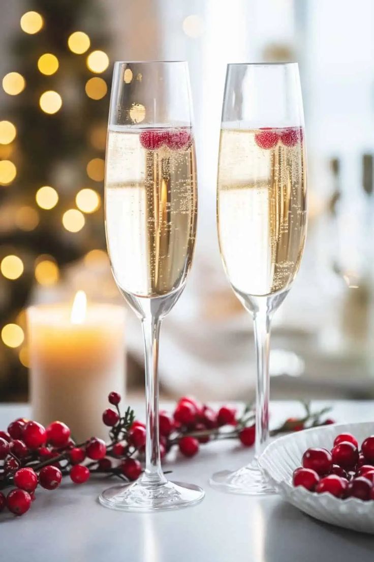 two glasses of champagne sitting on top of a table next to a candle and christmas decorations