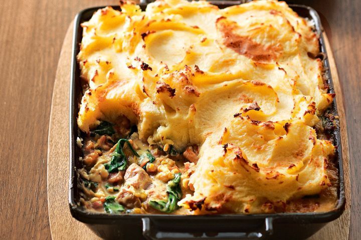 a casserole dish with meat, cheese and spinach in a black pan