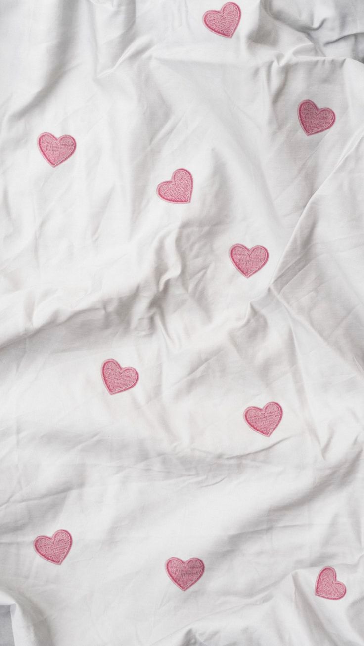 a bed with pink hearts on it and white sheets in the foreground, all over