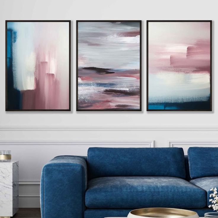 three paintings hang on the wall above a blue couch in a living room with white walls