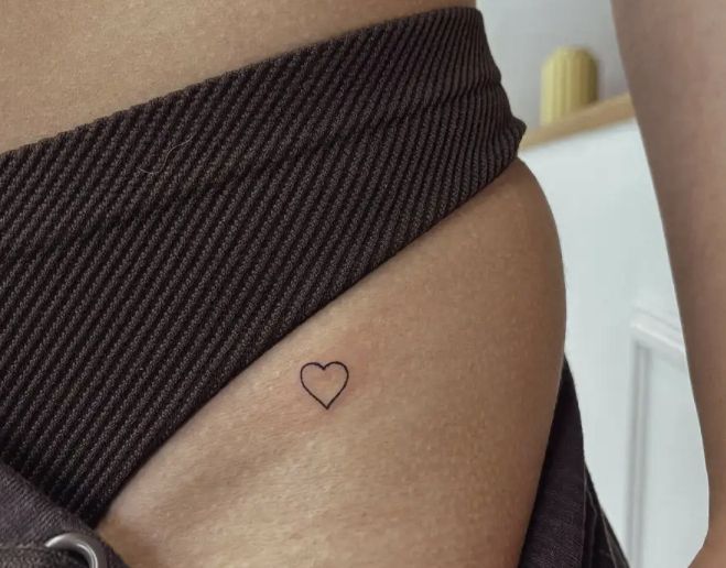 a woman's stomach with a small heart tattoo on her left side ribcage