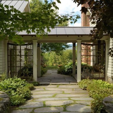 a stone walkway leading to a house with trees in the back ground and bushes on either side