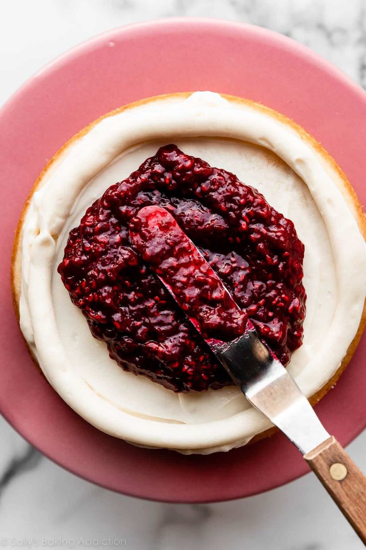 a red plate topped with cake covered in white frosting and raspberry topping