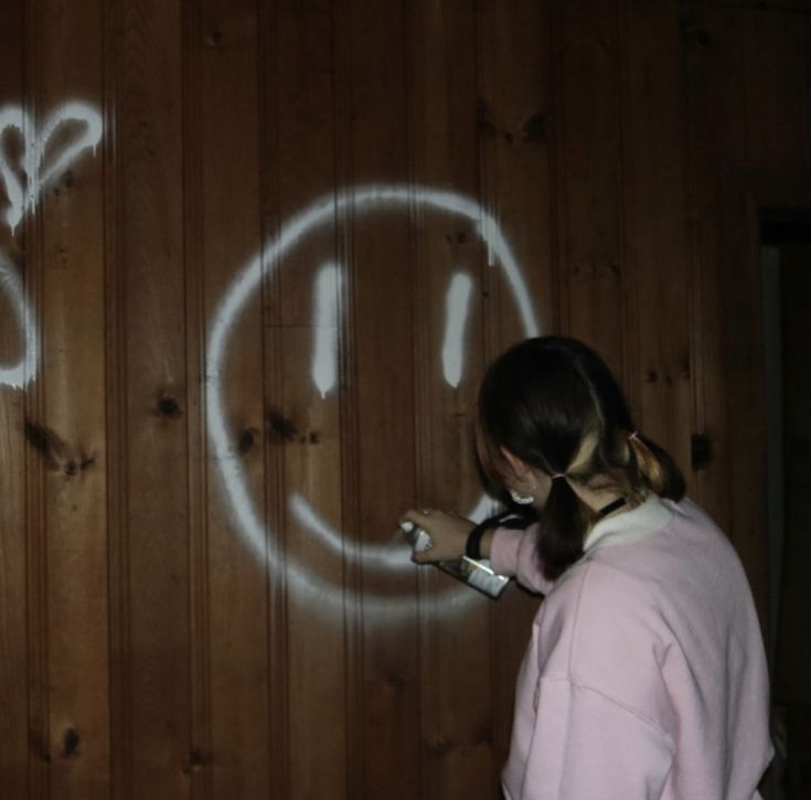 a girl is writing on the wall with white spray paint and has her face drawn onto it