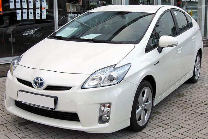 a white toyota prius parked in front of a glass storefront on a brick sidewalk