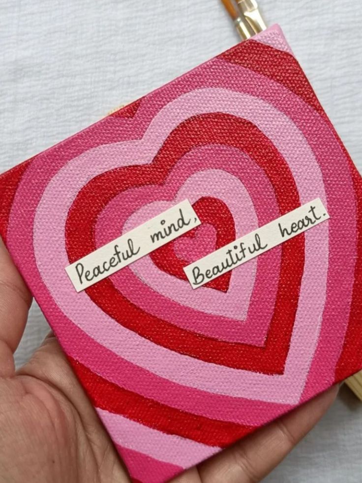 a hand holding a pink and red heart shaped painting with words written on the side