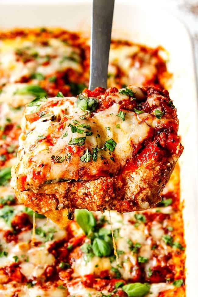 a close up of a piece of meat covered in sauce and herbs being lifted from a casserole dish