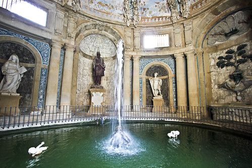 two white swans are swimming in the water inside an ornate building with statues on either side