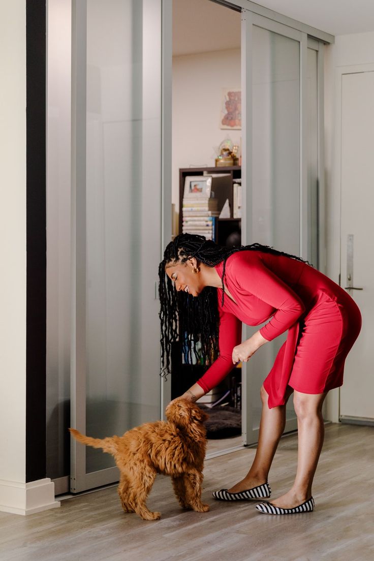 a woman is playing with her dog in the living room while wearing red pants and slippers