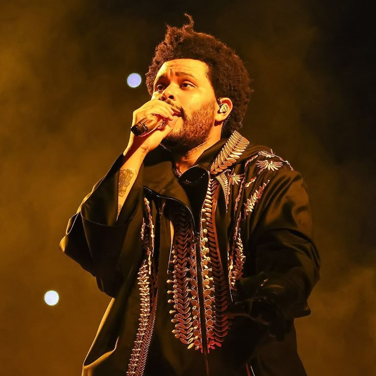 a man that is standing up with a microphone in his hand and some lights behind him