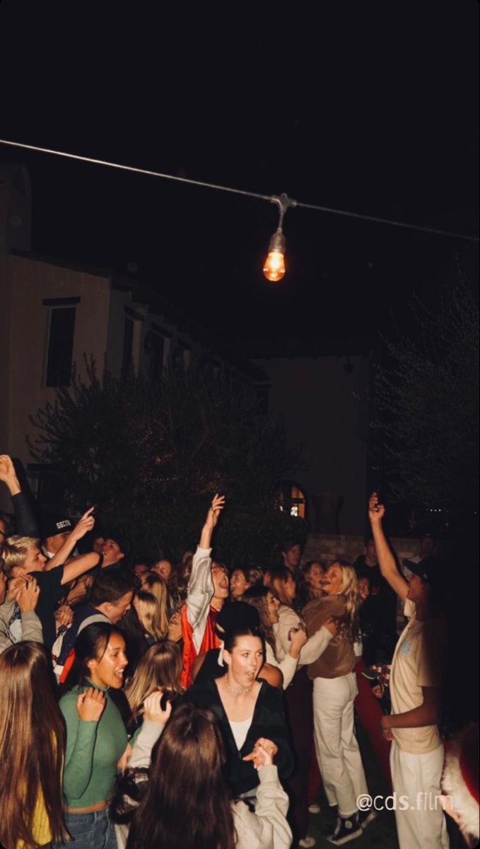 a group of people standing around each other in front of a building at night time