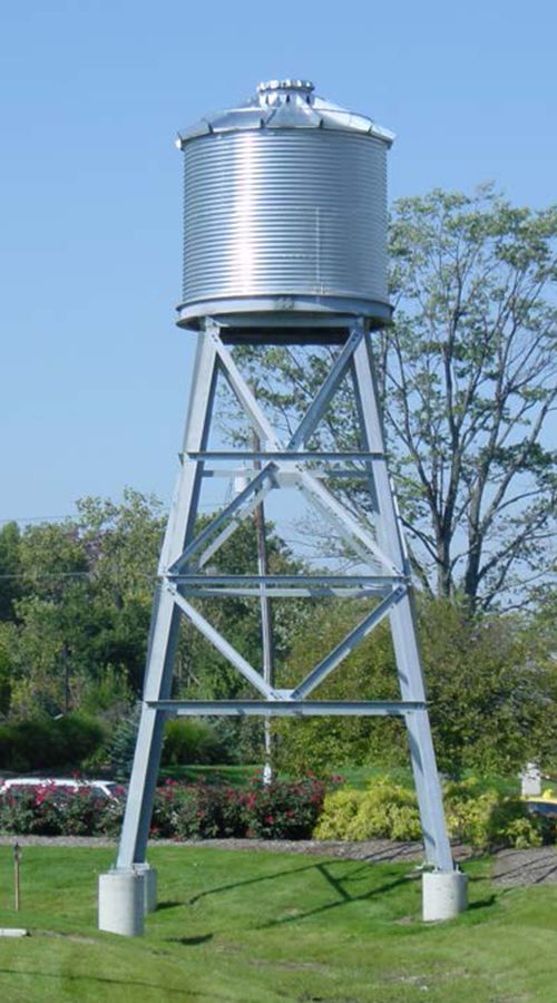 a large metal water tower sitting on top of a lush green field