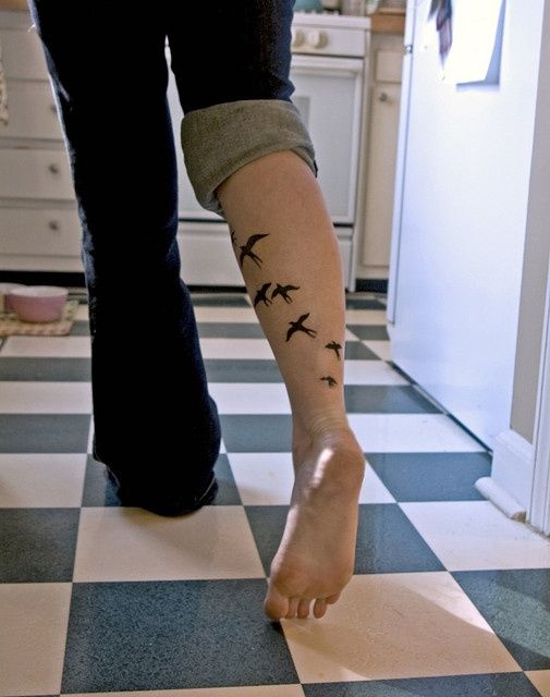 a woman's foot with birds on it in the middle of a checkered floor