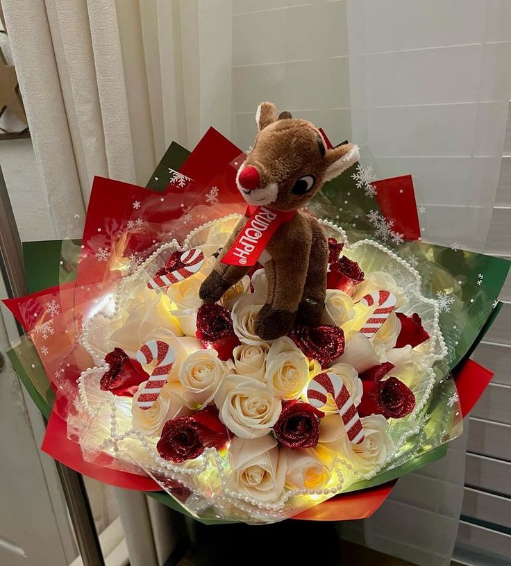 a teddy bear sitting on top of a bouquet of white and red frosted roses