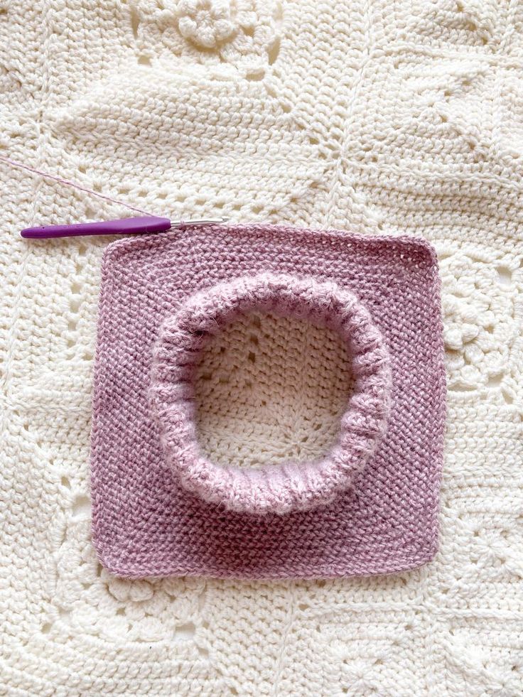 a crocheted square with a hole in the middle and a purple yarn needle