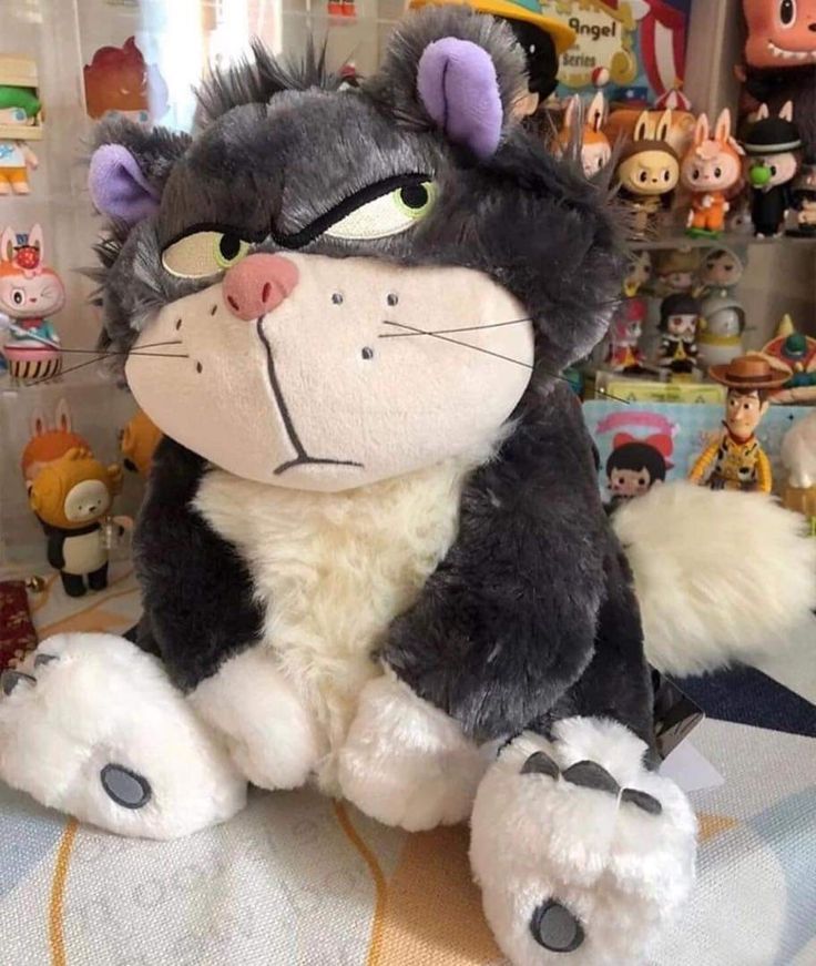 a large stuffed cat sitting on top of a bed next to other stuffed animals and toys