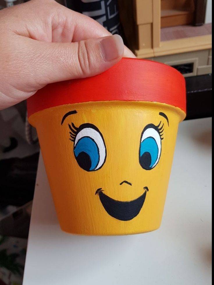 a hand holding a yellow cup with blue eyes and smiling face on the top,