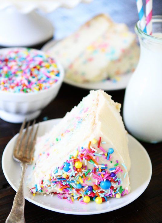 a slice of cake with sprinkles on a plate next to a glass of milk