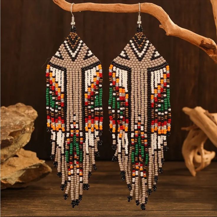 a pair of beaded earrings hanging from a wooden branch on top of a table