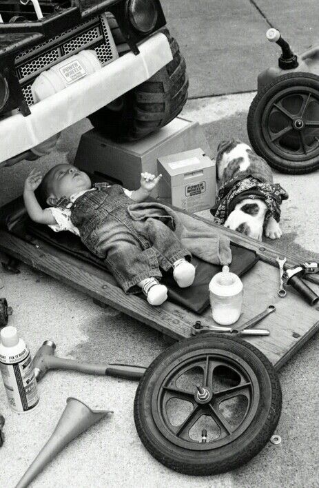 a small child laying on top of a wooden cart next to a car and tools