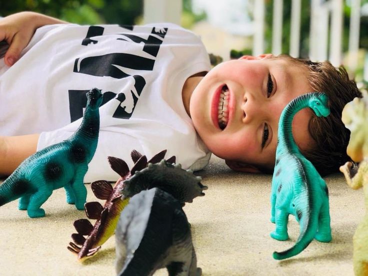 a young boy laying on the ground next to toy dinosaurs