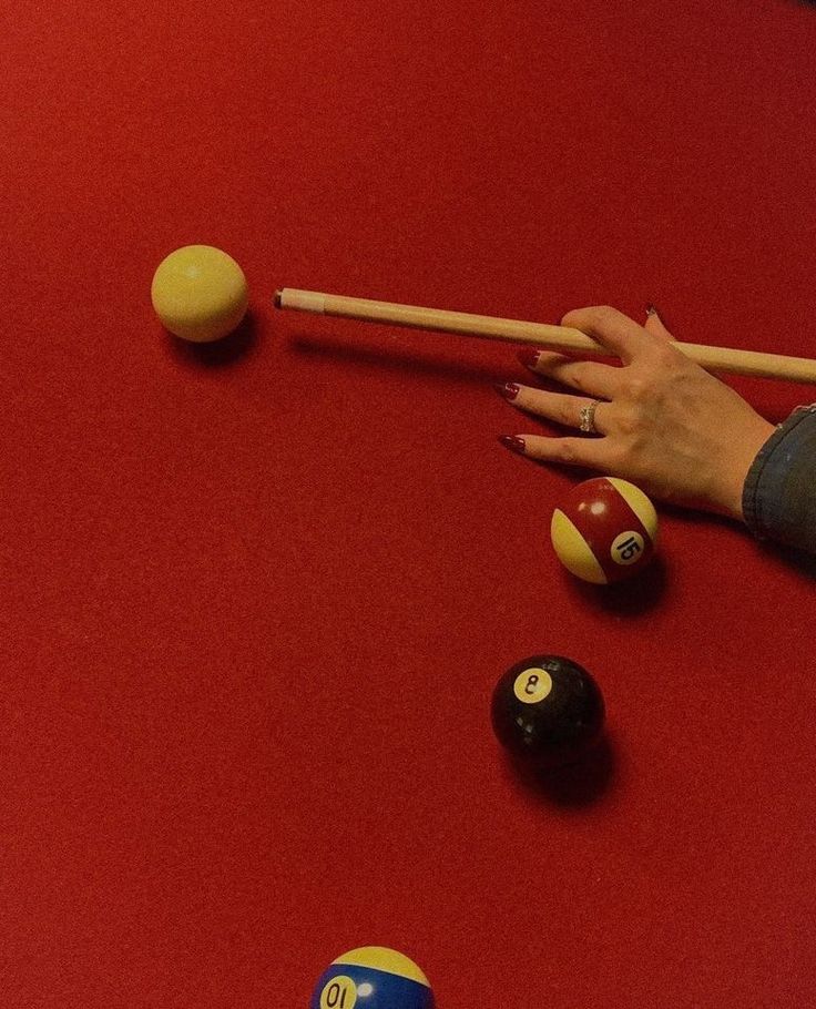 a woman's hand reaching for pool balls on a red table with cues