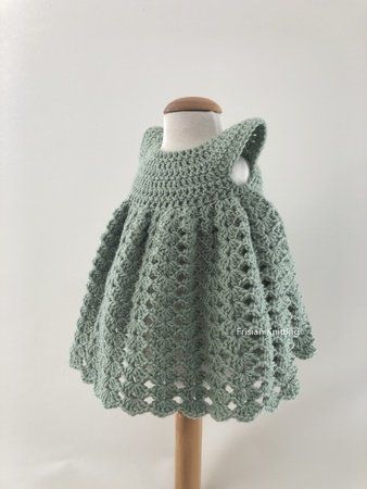 a green crocheted dress on a wooden mannequin with a white background