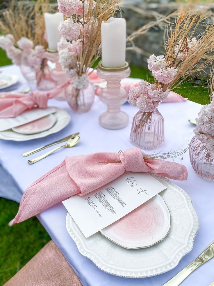 the table is set with pink napkins, plates and silverware in vases