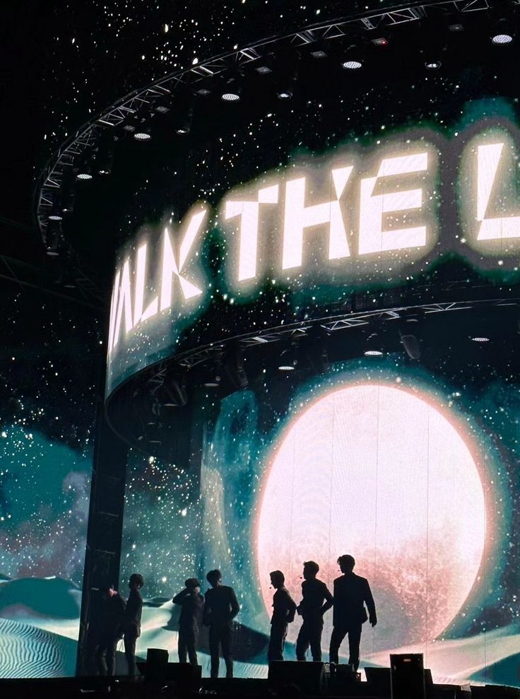 a group of people standing on top of a stage next to a giant neon sign