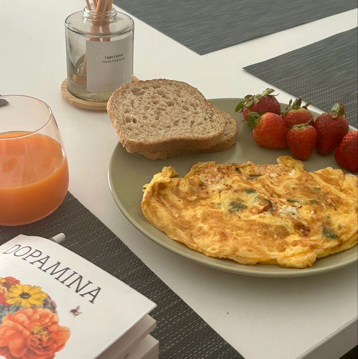 an omelet with toast, strawberries and juice on a table next to books