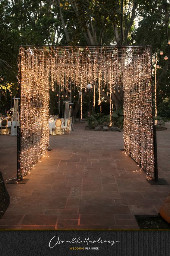 an outdoor wedding venue decorated with string lights and chandelier draped over the walkway