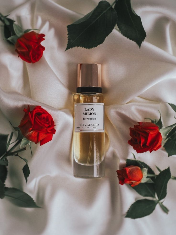 a bottle of perfume sitting on top of a white sheet with red roses around it