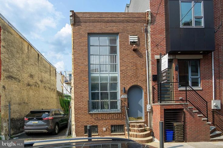 a car parked in front of a brick building on a street with stairs leading up to the second floor