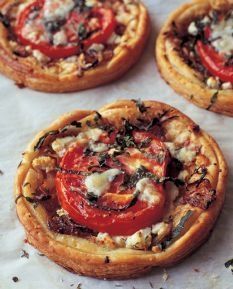 four small pizzas with tomatoes and cheese on them sitting on top of parchment paper