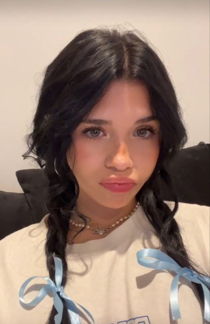 a woman with long black hair wearing a white shirt and blue ribbon around her neck