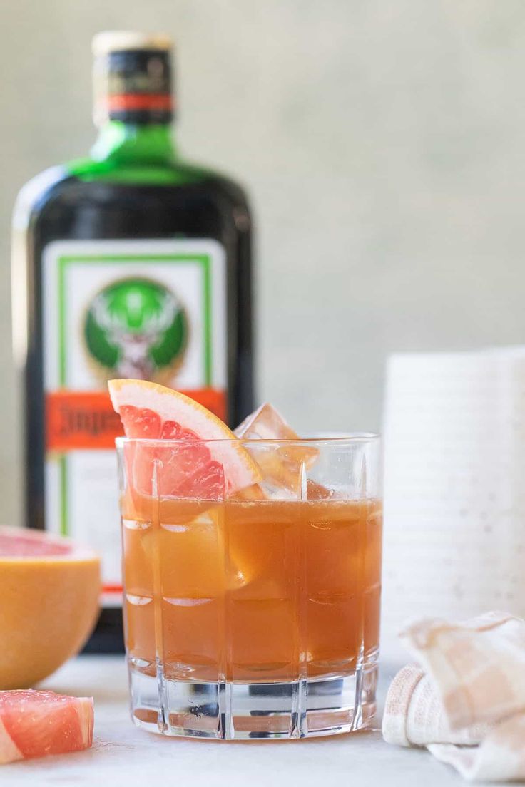 a glass filled with orange juice and garnished with an orange slice next to a bottle