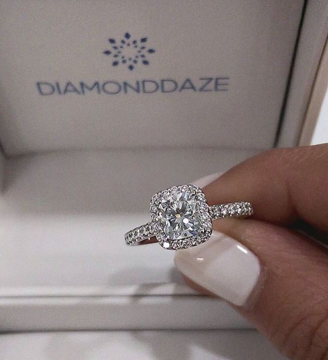 a woman's hand holding a diamond ring in front of a white box with diamonds on it